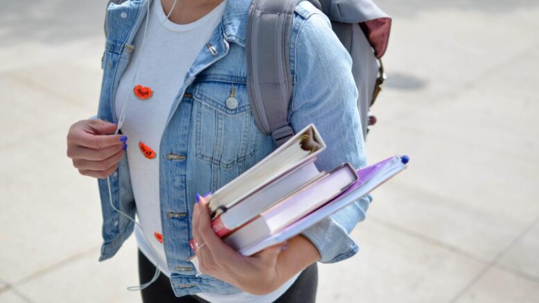 A picture of a medical student holding their books and walking to class with their backpack on